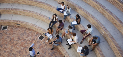 Students having class with book and tablets, in outside auditorium. Students with raised hands